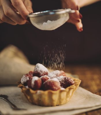 close-up-woman-dusting-sugar-powder-strawberry-tart